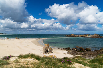 Plage de sable blanc et eaux turquoise sous un ciel bleu éblouissant parsemé de nuages blancs sur la côte bretonne.