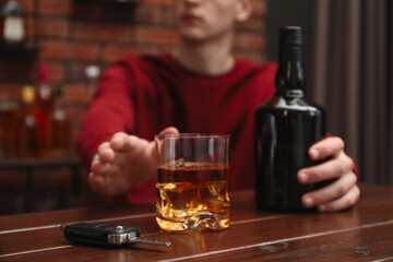 Man reaching for alcoholic drink at table with car keys, closeup. Don't drink and drive concept