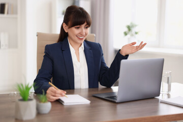 Woman taking notes during webinar at wooden table indoors