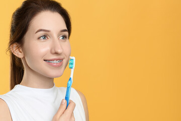 Portrait of smiling woman with dental braces and toothbrush on yellow background. Space for text
