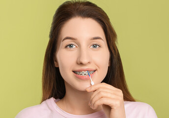 Smiling woman with dental braces cleaning teeth using interdental brush on light green background