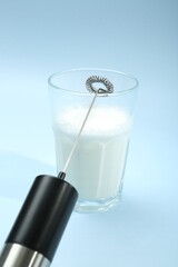 Mini mixer (milk frother) and whipped milk in glass on light blue background