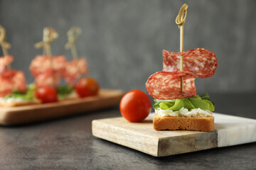 Tasty canapes with salami, greens, cream cheese and tomatoes on grey table, closeup. Space for text