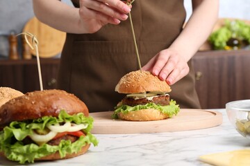 Woman making delicious vegetarian burger at white marble table, closeup