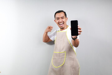 Asian handsome asian barista man wearing apron pointing finger at mobile screen, showing app and...