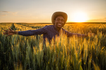 Portrait of african farmer in his growing wheat field. He is satisfied with progress of plants.