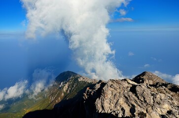 a hill covered in lots of mountains and clouds with a small white cloud sticking out