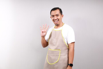 Happy Asian male housekeeper chef cook baker man wear apron showing four fingers isolated on gray...