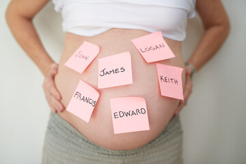 Baby names, belly and sticky notes with pregnant woman in studio on gray background for choice...