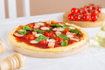 Handmade, DIY fresh pizza with ham, tomatoes, mozzarella, green and oil on a table in kitchen. Homemade pizza.