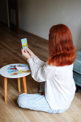 girl with red hair serious hold tarot cards, sit back to camera