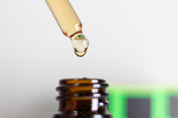 Close-Up Of Dropper With Liquid Over Brown Bottle. A close-up image showcasing a dropper releasing a droplet of liquid into a brown glass bottle. 