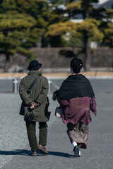 An elderly Japanese couple walks calmly along the paths of a park near the Imperial Palace in Tokyo on a sunny winter day