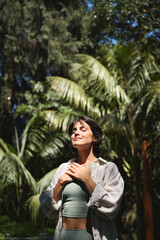 Happy calm young Hispanic woman holding hands on chest meditating doing yoga breathing exercises...