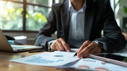 A professional in a suit reviews data charts and financial reports at a desk with a laptop and calculator