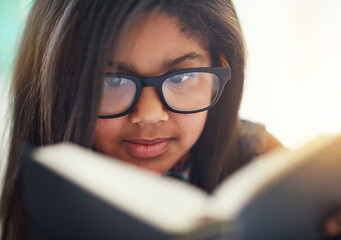 Child, girl and reading book in glasses for home learning, education or story with knowledge, smart...