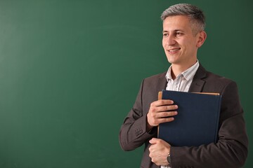 Teacher with notebooks near chalkboard, space for text