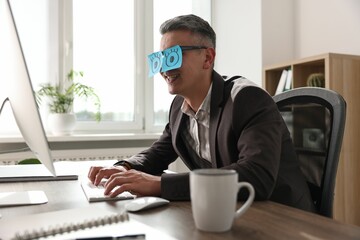 Man with fake eyes painted on sticky notes working on computer at table in office
