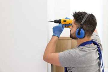 Young worker in uniform using electric drill indoors. Space for text