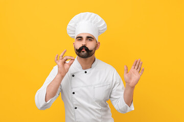 Professional chef with funny artificial moustache showing perfect sign on yellow background