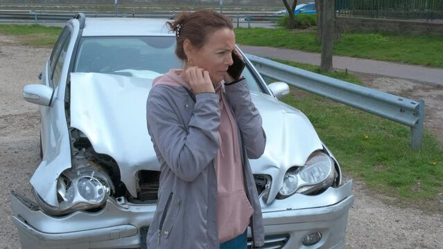 Call phone near crash incident. A view of worryed woman call for help by the smashed car in the street. A concept of car accident with woman driver.