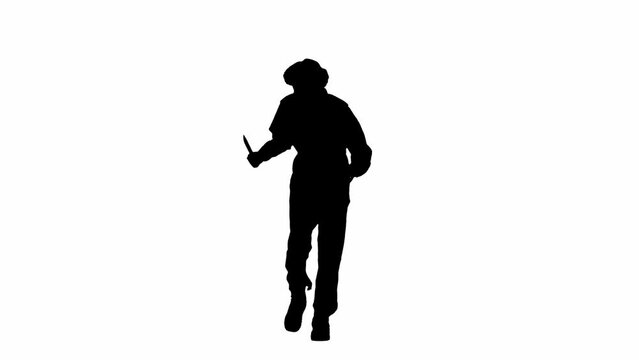 Black silhouette of a maniacal man in overalls walking with a knife in his hand and looking around. Unrecognizable man with curly hair on white isolated background.