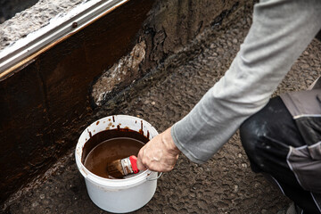 man applying primer with a brush to a damaged bitumen coating