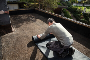 A craftsman rolls out a thick rubber tarpaulin on a flat roof