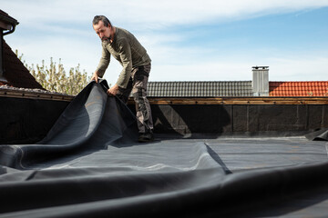 A craftsman rolls out a thick rubber tarpaulin on a flat roof