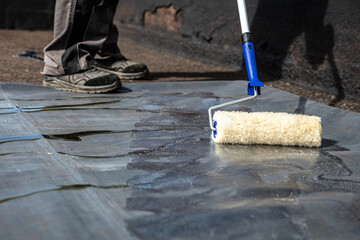 man applies adhesive to an old bitumen sealant and then glues on a rubber sheet