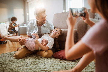 Father Playing with Daughter on Living Room Floor While Mother Takes Photo