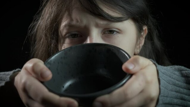 Child need for food with empty bowl. A view of young girl with empty bowl need for food against black background.