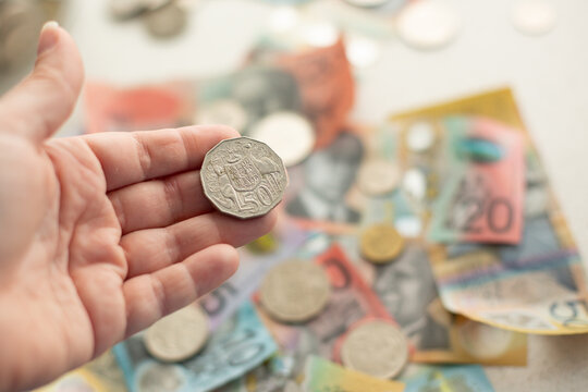 person holding an Australian 50 cent piece with other money in the background