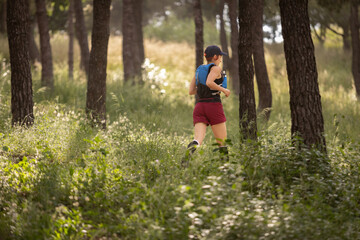 A woman is running through a forest with a backpack on. Scene is peaceful and serene, as the woman is surrounded by nature and the trees