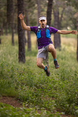 A man in a purple shirt and blue shorts is jumping in the air. He is wearing a blue hat and a blue backpack