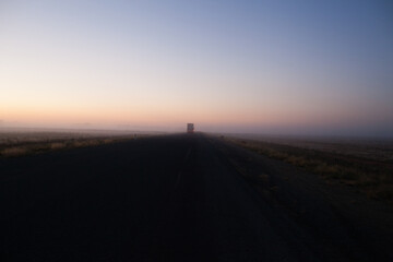 Country highway at sunrise with semi trailer truck driving off in distance