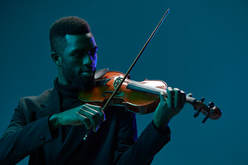 Elegant African American man in suit playing violin on blue background creating beautiful music and...