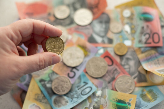 person holding a dollar coin between fingers with other money in the background