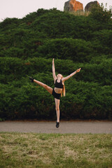 Little blonde girl in black top and shorts doing splits in the air on nature background. Sport and health lifestyle. Dancing girl