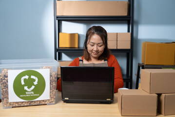 A woman working on a laptop managing online orders and eco-friendly packaging from water hyacinth...