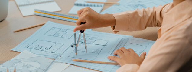 Professional architect drawing blueprint by using divider on the table with stationary and...