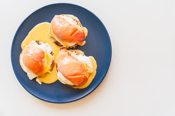 Toast with eggs benedict, salmon and hollandaise sauce on a blue plate on a white background. Space...