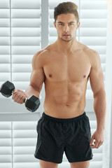 Obraz premium Muscular man, portrait and weightlifting with dumbbell for fitness, strength or muscle gain at home. Active male person or bodybuilder with small weight for workout, exercise or training at house