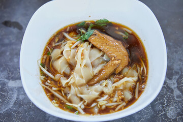 Wide rice noodles with braised chicken meat  in a bowl