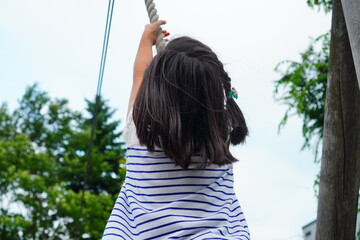 ターザンロープで遊ぶ小学生の頃3年生の女の子の後ろ姿