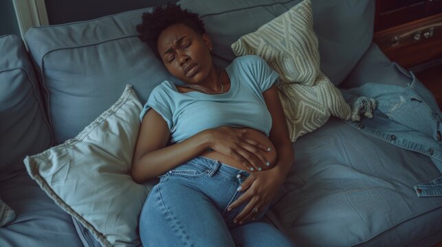 Period, stomach discomfort, and black woman clutch tummy on sofa from sickness, cramps, and digestion. Periods, endometriosis, and female on couch with pms and bloated belly