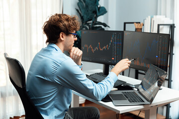 Young investor in stock trader pointing on dynamic exchange rate on laptop and pc screen in dynamic...