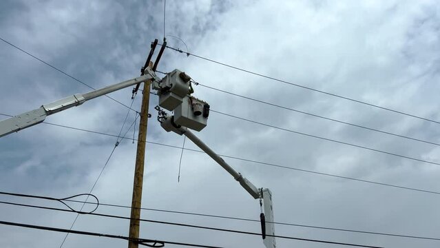Power line work. Lineman crews work on power lines high in the sky. An elevated hydraulic bucket lifts the workers up to the power line. Overcast cloudy skies.