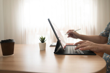 A woman is typing on a laptop with a pen in her hand
