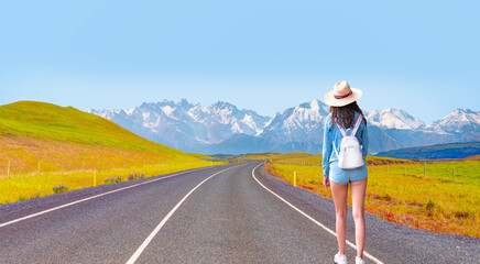 A young woman walking on a long asphel road towards the mountains